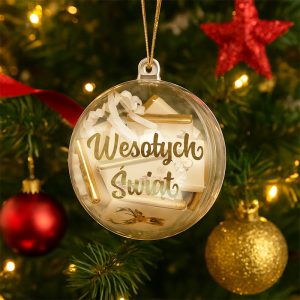 Przezroczysta bombka zawieszona na choince, wypełniona małymi, złotymi i białymi dekoracjami oraz napisem 'Wesołych Świąt' widocznym na froncie, w tle zielone gałęzie choinki z iluminacjami i innymi ozdobami.