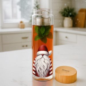 Przezroczysta butelka z herbatą, w której unoszą się świeże liście mięty; w tle widoczny jest rysunek postaci Świętego Mikołaja z biało-czerwonymi paskami, siedzącego na dnie butelki; na stoliku obok znajduje się drewnopodobna nakrętka z napisem 'RENATA'.