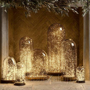 Sześć szklanych kloszy o różnych rozmiarach, wypełnionych migoczącymi światłami, ustawionych na kamiennej powierzchni, w tle z dekoracyjną ścianą w jasnym kolorze.