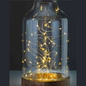 Szklany klosz z delikatnymi, świecącymi żarówkami wewnątrz, ustawiony na okrągłej drewnianej podstawie, tworząc ciepłą, przytulną atmosferę.