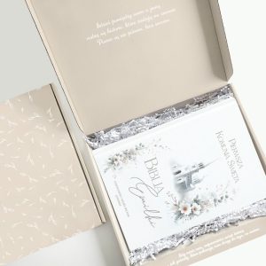 Otwarta, ozdobna pudełko zawierające białą Biblię z napisami, w tym "Pierwsza Komunia Święta" i delikatne kwiatowe wzory, otoczone srebrnym wypełnieniem; w tle widoczny cytat na wewnętrznej stronie wieka pudełka.