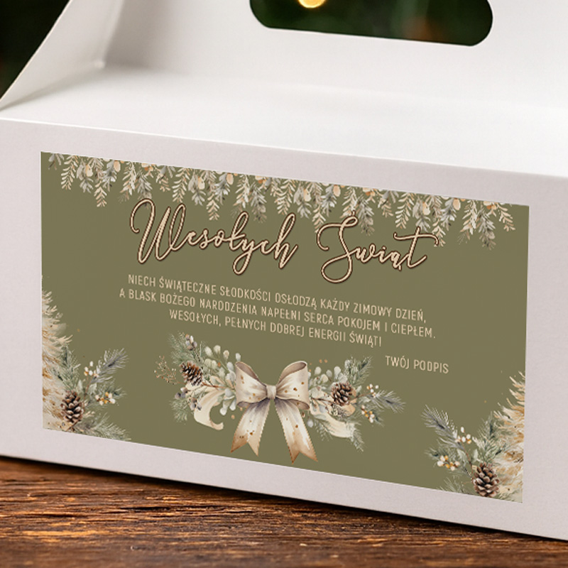 A decorative label on a white gift box, featuring the words 'Wesołych Świąt' in elegant script. The label is adorned with winter foliage, pine cones, and a bow, with a festive message in Polish wishing sweetness during the winter season and a joyful holiday spirit.