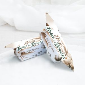 Dwa ozdobne pudełka z napisem "Dzień Babci i Dziadka" i datą "21/22 stycznia", leżące na jasnym tle, ozdobione delikatnymi motywami roślinnymi w pastelowych kolorach.