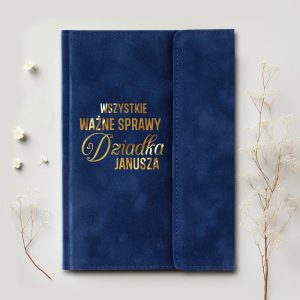 Niebieski notes z tytułem "WSZYSTKIE WAŻNE SPRAWY Dziadka Janusza" napisanym złotą czcionką, otoczony drobnymi kwiatami i gałązkami na jasnym tle.
