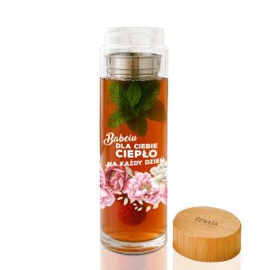 Szklanka do herbaty z naparem zawierającym miętę, z nadrukiem "Babciu dla Ciebie ciepło na każdy dzień" oraz różowym kwiatowym motywem u dołu, obok drewniana pokrywka z napisem "RENATA".