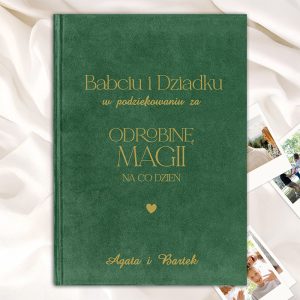 Okładka książki w zielonym kolorze, z tytułem 'Babci i Dziadku w podziękowaniu za ODROBINĘ MAGII NA CO DZIEŃ' napisanym złotą czcionką; w tle widoczne białe tkaniny oraz zdjęcia rodzinne.