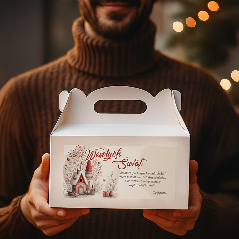 Mężczyzna trzyma białe pudełko z napisem 'Wesołych Świąt', które ma ilustrację domku i zimowe motywy. Tło jest przypominające świąteczny klimat, z miękkim światłem i rozmytymi dekoracjami.