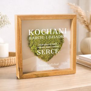 Tablica w drewnianej ramie z napisem 'KOCHANI BABCIU I DZIADKU' oraz sercem z mchu, z dodatkowym tekstem 'Dziękujemy za każdy cudowny dzień i wielkie SERCE' i datą '21.01.2026', ustawiona na stole w przytulnym wnętrzu.