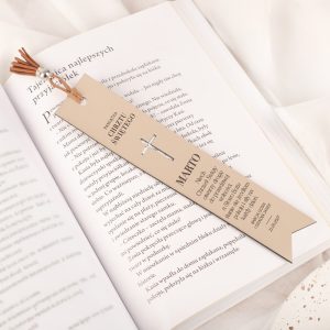 Zakładka do książki z napisem 'Pamiątka Chrzestu Świętego', ozdobiona krzyżem i frędzlami, leżąca na otwartej książce z tekstem w języku polskim.