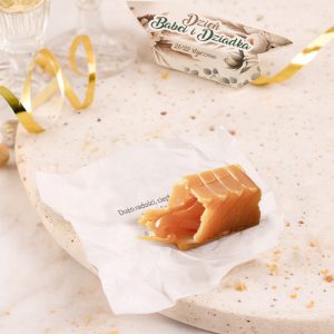 Mielony cukier na białym papierze, z widocznymi zębami, leży na jasnym podłożu. Obok znajdują się złote wstążki i kartka z napisem 'Dzień Babci i Dziadka', datą 21/22 stycznia.