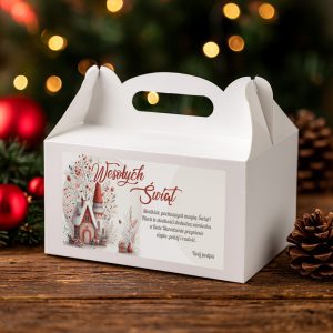 Swiateczne-pudelko-z-raczka-na-ciasto-bozonarodzeniowe Biała pudełko na świąteczne prezenty z napisem 'Wesołych Świąt' oraz ilustracją świątecznego domku i dekoracji, umieszczone na drewnianym stole w tle z gałązkami i bombkami.