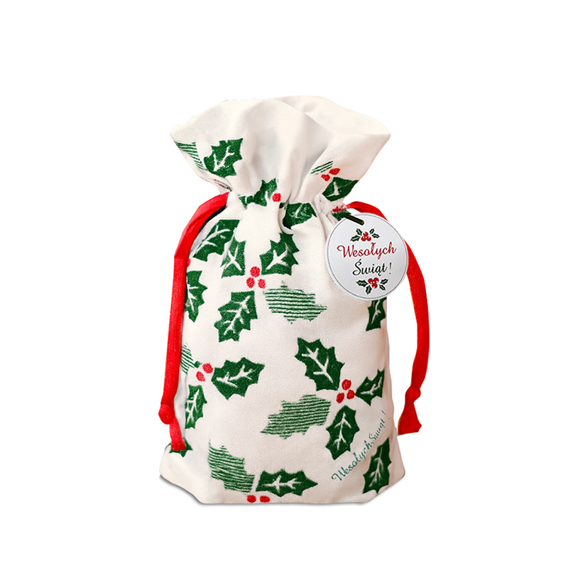 Mały woreczek świąteczny wykonany z białego materiału, ozdobiony zielonymi liśćmi ostrokrzewu i czerwonymi jagodami, z czerwonymi sznurkami do związania oraz okrągłą etykietą z napisem 'Wesołych Świąt!'.