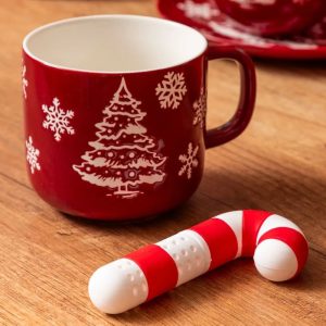 Czerwona filiżanka z białymi wzorami bałwanków i śnieżynek, obok znajduje się cukierek w kształcie laseczki w paski czerwono-białe, na drewnianym blacie.