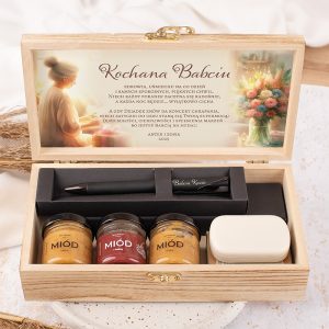 Drewniane pudełko z napisem "Kochana Babciu" oraz zestawem prezentowym, zawierającym słoiczki z miodem i długopisem, a także kartkę z życzeniami i ilustracją kwiatów w tle.