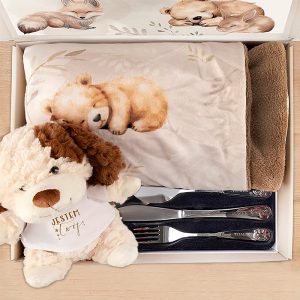 Pudełko zawierające miękką kocyk z nadrukiem niedźwiadka, pluszowego psa w białej koszulce z napisem 'JESTEM CUDNY', oraz zestaw srebrnych sztućców.
