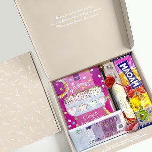 Otwarta pudełko zawierające różne słodycze, w tym zestaw DIY do robienia biżuterii z cukierków, batoniki, cukierki, chipsy oraz banknot 500 euro na dnie oferty.