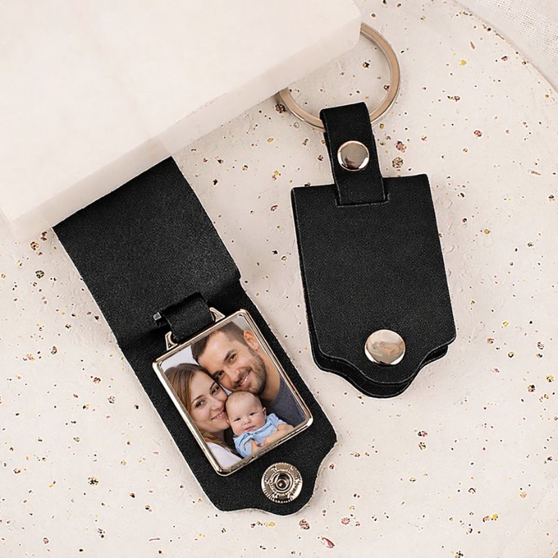 Czarny brelok do kluczy z metalowym uchwytem, w którym umieszczone jest zdjęcie rodziny składającej się z matki, ojca i dziecka.