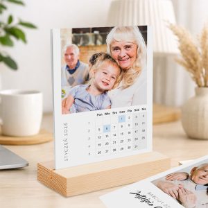 Kalendarium na stoliczku z zdjęciem starszej kobiety przytulającej małą dziewczynkę, w tle widoczna para ludzi; na dole kalendarza miesiąc styczeń 2026, w formacie cyfrowym z zaznaczoną datą 6.