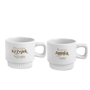 Dwie białe filiżanki z napisem: po lewej 'Dziadek Krzysiek wie wszystko', po prawej 'Babcia Janinka wie lepiej', prezentujące rodzinny motyw.