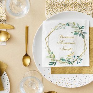 Stół nakryty na uroczystość, z białym talerzem ozdobionym złoconym napisem 'Pierwsza Komunia Święta' na serwetce, złotymi sztućcami, przezroczystą szklanką oraz dodatkową złotą serwetką obok.