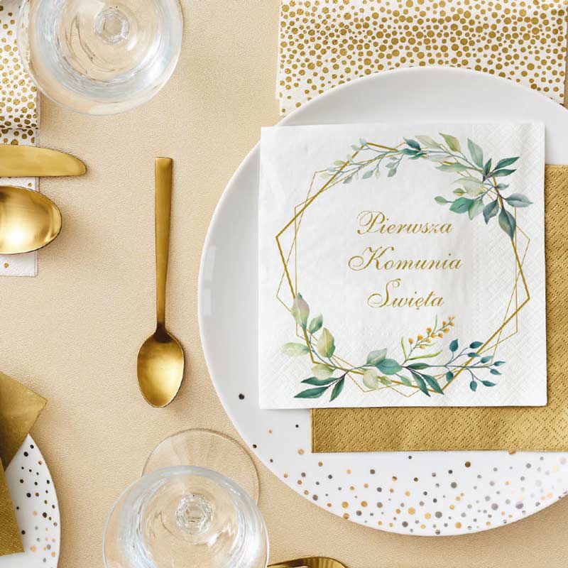 Stół nakryty na uroczystość, z białym talerzem ozdobionym złoconym napisem 'Pierwsza Komunia Święta' na serwetce, złotymi sztućcami, przezroczystą szklanką oraz dodatkową złotą serwetką obok.