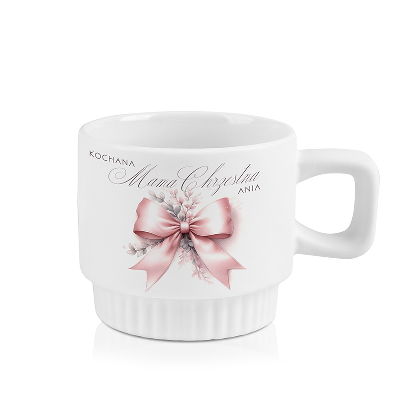 Biała filiżanka ozdobiona różową wstążką i kwiatami, z napisem 'KOCHANA Mama Chrzestna ANIA' na boku.