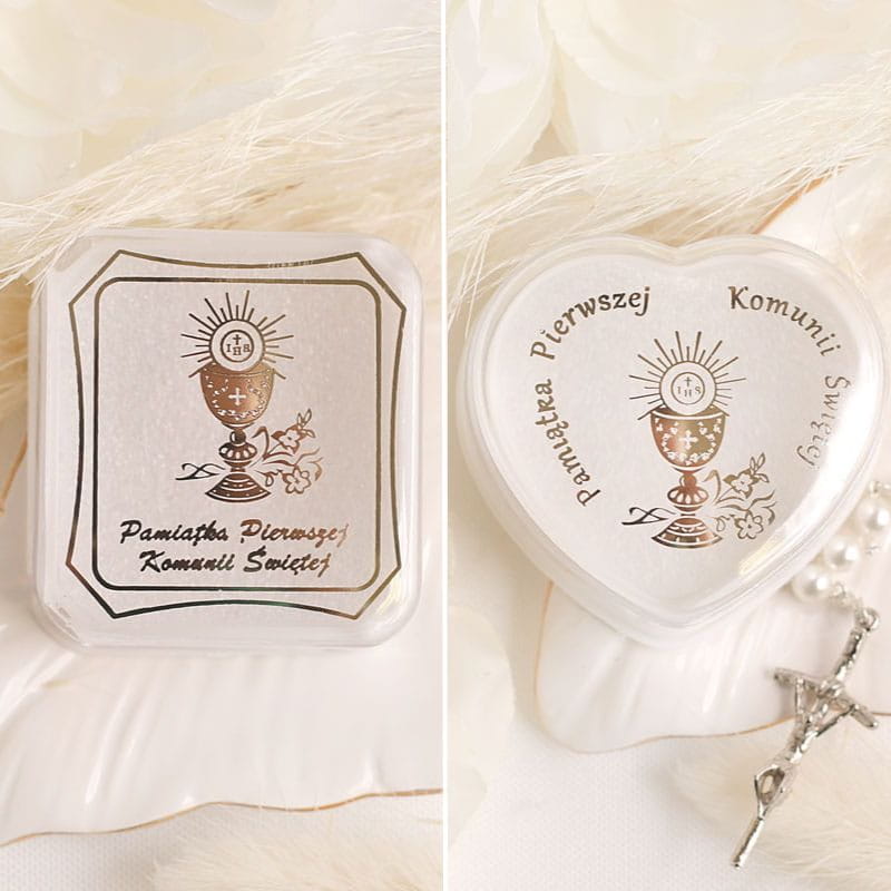 Dwa opakowania pamiątek Pierwszej Komunii Świętej, jedno o prostokątnym kształcie z motywem kielicha i napisem 'Pamiątka Pierwszej Komunii Świętej', drugie w kształcie serca z podobnym motywem i napisem 'Pamiątka Pierwszej Komunii Świętej'. Tło delikatne, z białymi kwiatami i biżuterią religijną.