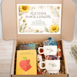 Otwarta kartonowa paczka z prezentem, zawierająca książki, dwa kubki z imionami "Babcia Jola" i "Dziadek Bronisław", słodycze oraz szalik, z ozdobnym liściastym nadrukiem na wieczku z napisem "Kochani Babciu i Dziadku".