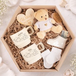 Zestaw prezentowy zawierający dwa kubki z napisami "Mama" i "Tata", małego misia, skarpetki oraz drewniane serce z napisem.