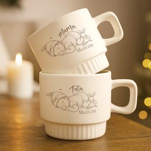 Dwa ceramiczne kubki z rysunkami noworodków, jeden z napisem "Mama", a drugi "Tata", ustawione jeden na drugim.
