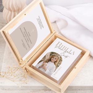 Książka Biblia w drewnianej skrzynce, otwarta, z wizerunkiem dziewczynki w białej sukience i kwiecistym nakryciu głowy.