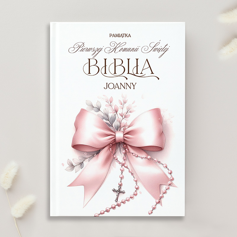 Okładka książki z tytułem "Biblia Joanny" na białym tle, ozdobiona różową wstążką i delikatnymi elementami roślinnymi w pastelowych kolorach, z koralikami i krzyżykiem zawieszonym na wstędze.