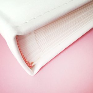 Zdjęcie grzbietu białej książki na różowym tle, z widocznymi egzemplarzem kartkowym i delikatnymi detalami wykończenia.