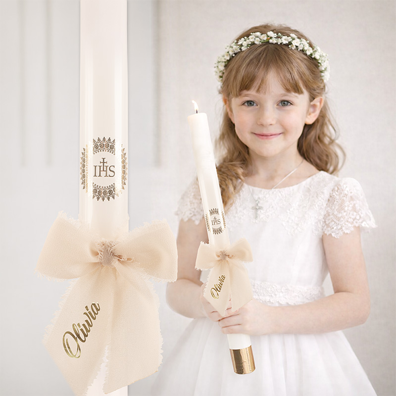 Dziewczynka w białej sukience z krótkim rękawem trzyma świecę zdobioną wstążką, wygląda na przygotowaną do ceremonii.