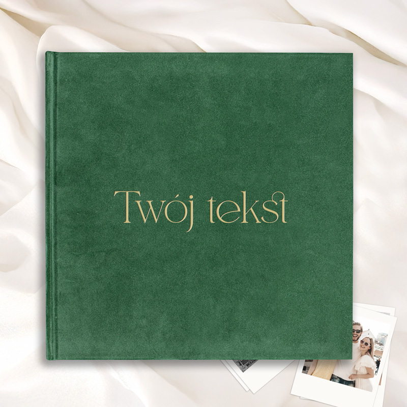 Zielona okładka książki z napisem "Twój tekst" w złotym kolorze, leżąca na jasnym tle z fałdami materiału i zdjęciami.