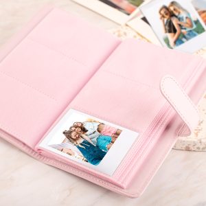 Różowa fotoksiążka otwarta, z jedną zdjęciem przedstawiającym trzy uśmiechnięte dziewczyny w środku. W tle inne zdjęcia.