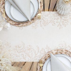 Stół z bieżnikiem w kwiatowy wzór, talerzami i serwetkami w pastelowych odcieniach oraz plecionymi podkładkami.