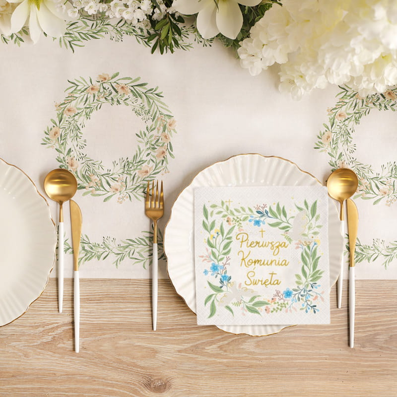 Stół udekorowany białym obrusem z kwiatowymi wzorami, talerze z eleganckimi sztućcami i serwetka z napisem "Pierwsza Komunia Święta".