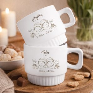 Białe filiżanki z napisem "Mama" i "Tata", na których znajdują się rysunki dzieci z królikami, na drewnianym stole.