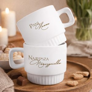 Dwie białe filiżanki z eleganckim, złotym napisem: imieniem i "Najlepsza Nauczycielka". W tle świeczki i smakołyki.