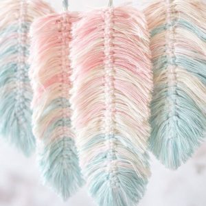 Trzy pękate dekoracyjne pióra w pastelowych kolorach: różowym, niebieskim i kremowym, wykonane z włóczki.