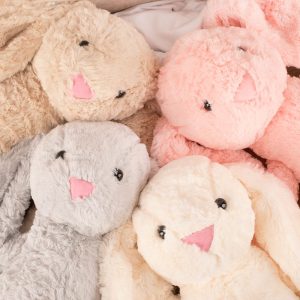 Cztery pluszowe króliczki w różnych kolorach: beżowym, różowym i szarym, leżą obok siebie na miękkim tle.