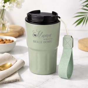 Stylowy kubek termiczny w kolorze zielonym z czarną pokrywką, oznaczony napisem "Mama SERCE DOMU," z praktyczną zawieszką.