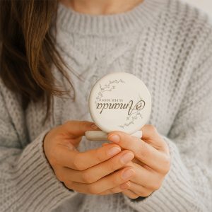 lusterko-na-dzien-mamy.jpg Osoba trzyma okrągłe opakowanie kosmetyczne w delikatnej scenerii.