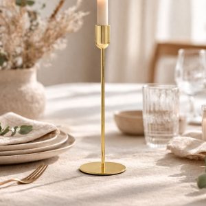 Złoty świecznik na długiej nóżce stojący na eleganckim obrusie, otoczony naczyniami i dekoracjami stołowymi.