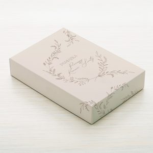 Eleganckie, jasne pudełko z napisem "Pamiątka" i delikatnym, roślinnym wzorem.