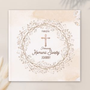 Okładka książeczki z napisem "Pamiątka Pierwszej Komunii Świętej", otoczona delikatnym wieńcem z białych kwiatów.