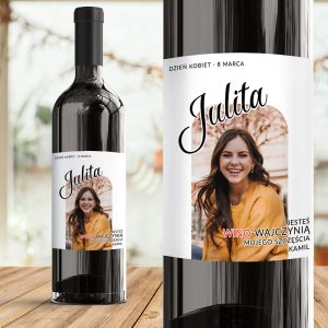 Butelka wina z etykietą z imieniem, na której znajduje się zdjęcie uśmiechającej się kobiety w żółtej bluzie, z tekstem z okazji Dnia Kobiet.