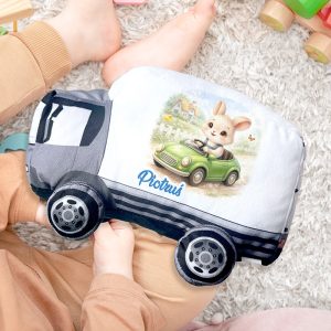poduszka-w-ksztalcie-ciezarowki.jpg Poduszka w kształcie samochodu z króliczkiem za kierownicą, imieniem na boku, otoczona zabawkami.