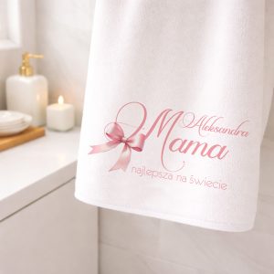 Biały ręcznik z różowym napisem "Mama najlepsza na świecie" oraz imieniem, zawieszony w łazience.